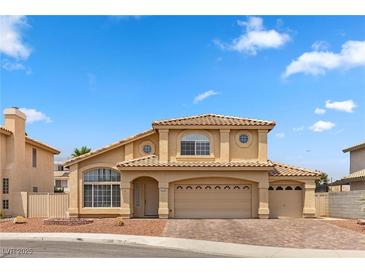 Two-story home with tan stucco exterior, tile roof, brick driveway, and three-car garage at 2716 Timber Crossing Ct, Henderson, NV 89074