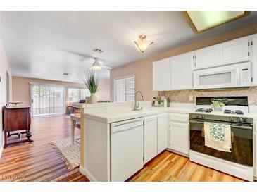Well-lit kitchen featuring white cabinets, appliances, and a breakfast bar overlooking the adjacent living area at 3125 N Buffalo Dr # 1091, Las Vegas, NV 89128