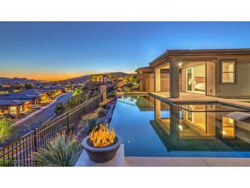 This backyard has a beautiful pool, fire pit, and mountain views with a bedroom visible through the glass door at 51 Reflection Cove Dr, Henderson, NV 89011