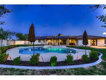 An in-ground pool is surrounded by landscaping and patio umbrellas at the rear of this well-maintained home at 2721 Family Ct, Las Vegas, NV 89117