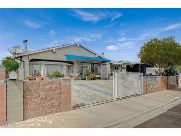 Charming single-story home featuring a gated front yard, covered entry, and mature trees under a bright blue sky at 405 Longtree Ave, Henderson, NV 89011