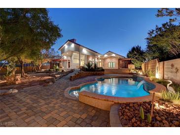 Stunning backyard oasis featuring a pristine pool with waterfall and desert landscaping at 8470 S Pioneer Way, Las Vegas, NV 89113