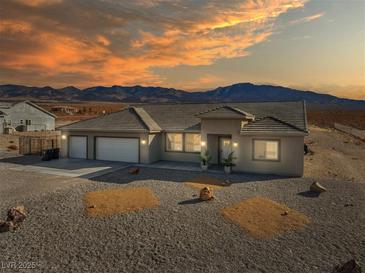 Charming single-story home with a three-car garage, desert landscaping, and mountain views at sunset at 6101 Cavalry Trl, Pahrump, NV 89060