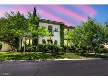 Elegant two-story home featuring lush landscaping, arched entryways, and a private balcony overlooking the front yard at 1409 Chambolle Ct, Las Vegas, NV 89144