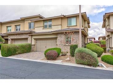 Charming townhouse with a tan exterior, brick accents, well-manicured landscaping, and a two-car garage at 10356 Addie De Mar Ln, Las Vegas, NV 89135