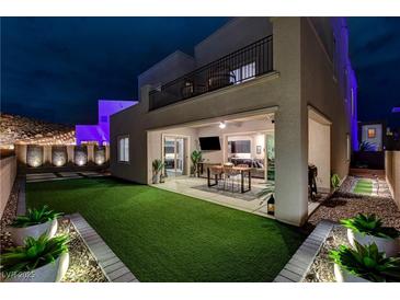 Beautiful backyard at night with a synthetic grass, covered patio, string lights and exterior uplighting at 746 Horizon Canyon Dr, Henderson, NV 89052