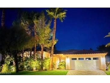 Beautiful single-story home with lush landscaping and a two-car garage, warmly lit against a night sky at 129 Chateau Whistler Ct, Las Vegas, NV 89148