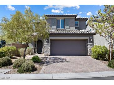 Charming two-story home featuring stone accents, gray siding, a brick driveway, and a two-car garage at 10925 Jordyn Hill St, Las Vegas, NV 89141