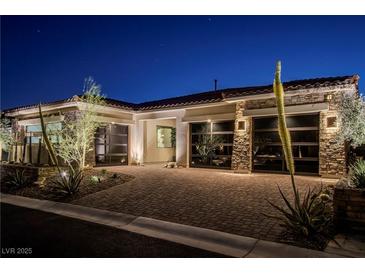 Striking home exterior featuring a stone facade and modern glass garage doors at twilight at 47 Garibaldi Way, Henderson, NV 89011