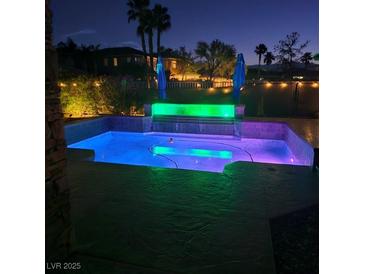 A backyard pool and waterfall feature illuminated by color-changing LED lights offers a relaxing outdoor retreat at night at 8209 Chapelle Ct, Las Vegas, NV 89131