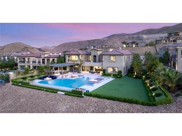 A gorgeous backyard boasts a modern pool, outdoor kitchen, fire features and lush landscaping set against a mountain backdrop at 34 Olympia Outlook Dr, Las Vegas, NV 89141
