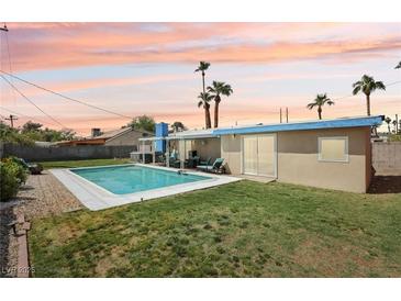 Inviting backyard with a sparkling pool, lush green lawn, and mature palm trees set against a colorful sky at 3140 Sundown Dr, Las Vegas, NV 89169