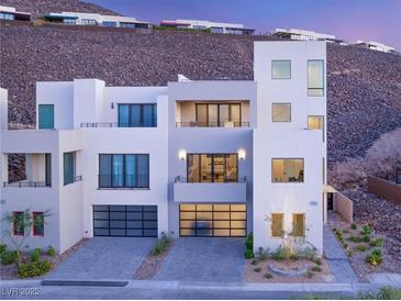 Modern home exterior featuring clean lines, multiple balconies, and glass garage doors nestled against a hillside at 394 Solitude Peak Ln, Henderson, NV 89012