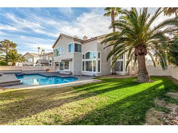 Spacious backyard features a sparkling pool, lush green lawn, and mature palm trees, perfect for outdoor living at 7900 Riviera Beach Dr, Las Vegas, NV 89128