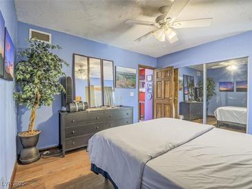 Cozy bedroom features wood floors, ceiling fan, and ample storage with mirrored closet at 438 Las Casitas Way, Las Vegas, NV 89121