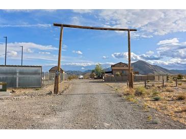 Gravel driveway leading to a ranch-style home under a rustic wooden archway with mountain views at 11875 Maggie Ave, Las Vegas, NV 89166