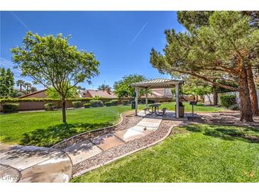 Inviting common area featuring covered picnic tables, barbecue grills, lush greenery, and mature trees under a clear blue sky at 8942 Galena Crossing St, Las Vegas, NV 89123