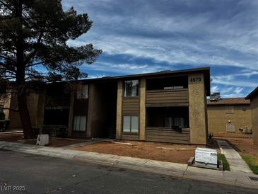 A tan two-story apartment complex featuring an open walkway and a large tree at 4570 Carriage Park Dr, Las Vegas, NV 89121