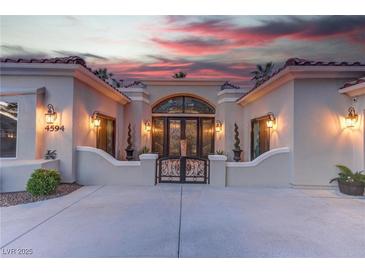 Elegant front entrance features a decorative metal gate and ornate double doors, set against a vibrant sunset backdrop at 4594 Blue Mesa Way, Las Vegas, NV 89129
