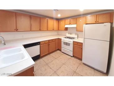 A functional kitchen includes wood cabinets, white countertops, and appliances on neutral tile floors at 9580 W Reno Ave # 183, Las Vegas, NV 89148