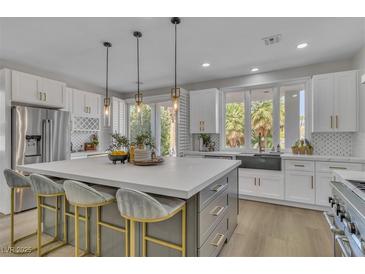 Bright kitchen boasts white cabinets, stainless appliances, large island with seating, and modern pendant lighting at 8848 Rainbow Ridge Dr, Las Vegas, NV 89117