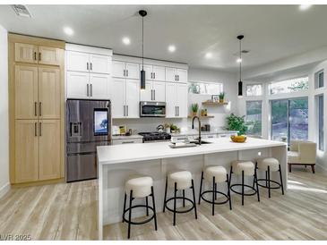 Bright, updated kitchen with white cabinets, a large island with seating, and modern stainless steel appliances at 10709 Hunters Woods Pl, Las Vegas, NV 89134