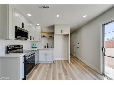 Updated kitchen featuring stainless steel appliances, modern white cabinets, and light wood flooring at 709 Rossmoyne Ave, North Las Vegas, NV 89030