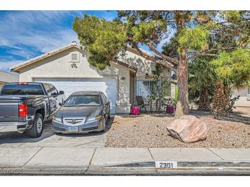 Charming single-story home featuring a two-car garage, desert landscaping, and mature shade tree at 2301 Cambridge Elms St, North Las Vegas, NV 89032