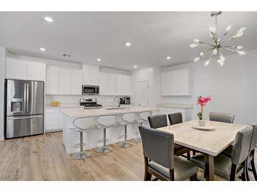 Bright kitchen features an island with seating, stainless steel appliances, and a dining area with modern light fixture at 4436 Mural Glen Ct, North Las Vegas, NV 89084