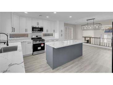 Modern kitchen features white cabinets, stainless steel appliances, and a gray kitchen island with marble countertops at 8232 Ocean Terrace Way, Las Vegas, NV 89128
