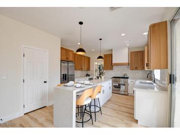 Bright kitchen with white marble island, modern appliances, wood cabinets, and stylish pendant lighting at 955 Leadville Meadows Dr, Henderson, NV 89052