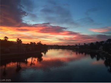 Scenic waterfront view with a vibrant sunset reflecting on the calm water and silhouetting the surrounding palm trees at 3125 N Buffalo Dr # 1080, Las Vegas, NV 89128