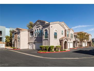 View of the exterior of the apartment complex with tan stucco, red trim, and a row of garages at 10001 Peace Way # 2228, Las Vegas, NV 89147