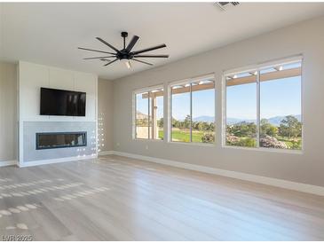 Bright living room featuring a fireplace, ceiling fan, and large windows with stunning golf course views at 2024 Bay Tree Dr, Las Vegas, NV 89134