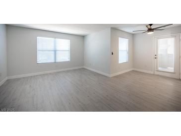 Bright living room featuring wood-look flooring, two windows, a ceiling fan, and a glass door at 5055 W Hacienda Ave # 2125, Las Vegas, NV 89118