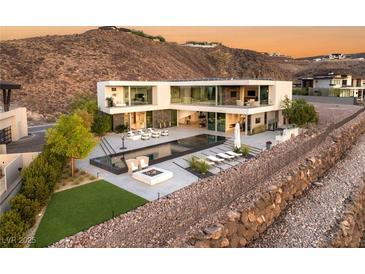 Modern home featuring a sleek pool, fire pit, and expansive glass walls against a mountainous backdrop at 13 Rockstream Dr, Henderson, NV 89012