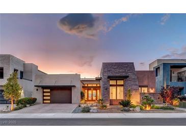 Stunning modern home featuring stone accents, lush landscaping, and a multi-car garage at dusk at 2180 Skyline Heights Ln, Henderson, NV 89052