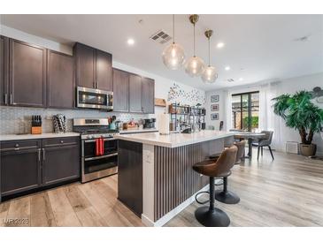 Modern kitchen features stainless appliances, white counters, backsplash, stylish island, and pendant lighting at 6141 May River St, Las Vegas, NV 89148