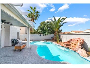 Backyard pool with rock waterfall feature, palm trees, and covered patio at 3695 Funston Way, Las Vegas, NV 89129