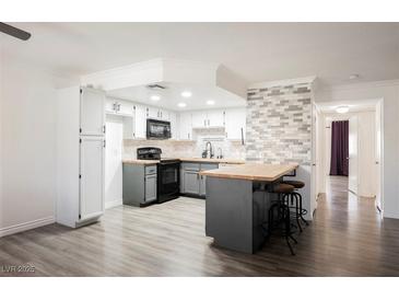Bright kitchen with wood floors, white cabinets, island with seating and accent tile at 1316 Driscoll Dr # 201, Las Vegas, NV 89128