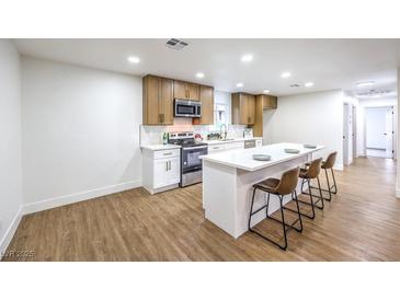 Modern kitchen features stainless steel appliances, white cabinets, quartz countertops, and an island with bar seating at 2536 Herrod Dr, North Las Vegas, NV 89030