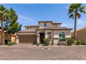 Charming two-story home with a tile roof, palm trees, and a brick driveway on a sunny day at 63 Via Di Mello, Henderson, NV 89011