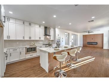 Modern kitchen features white cabinets, stainless steel appliances, an island with bar seating, and wood-look flooring at 1136 Casady Hollow Ave, Henderson, NV 89012