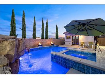 Inviting pool and spa featuring a rock waterfall, fire bowls, and lush landscaping create a serene backyard oasis at 12219 Crystal Shore Ave, Las Vegas, NV 89138