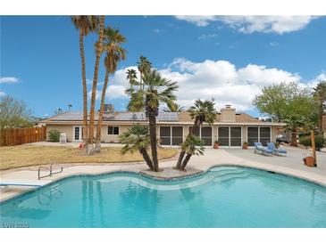 Backyard pool features a diving board and an inviting lounge area surrounded by swaying palm trees and blue skies at 3155 Duneville St, Las Vegas, NV 89146