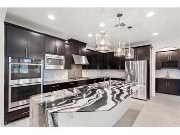 Modern kitchen featuring dark cabinetry, stainless steel appliances, and a waterfall edge island with marble-patterned countertop at 724 Step Beach St, Las Vegas, NV 89138