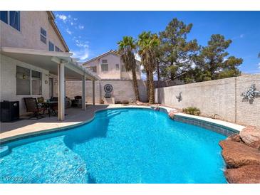 Sparkling pool with rock feature, covered patio, and lush landscaping create a backyard oasis at 9516 Belgate Ct, Las Vegas, NV 89129