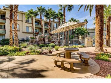 Community courtyard with picnic table, umbrella, rock waterfall, and lush desert landscaping by the pool at 7119 S Durango Dr # 303, Las Vegas, NV 89113
