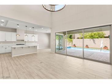 Bright living room showcasing a kitchen view and large sliding doors that open to a refreshing swimming pool area at 12048 Portamento Ct, Las Vegas, NV 89138