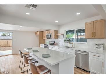 Bright kitchen features stainless steel appliances, white cabinets, quartz countertops, and an island with barstool seating at 40 Laswell St, Henderson, NV 89015